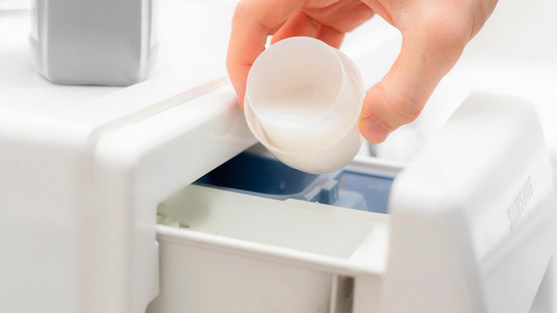 Eine Hand gibt aus einem Waschmittelverschluss Waschmittel in die Dosierkammer einer Waschmaschine.